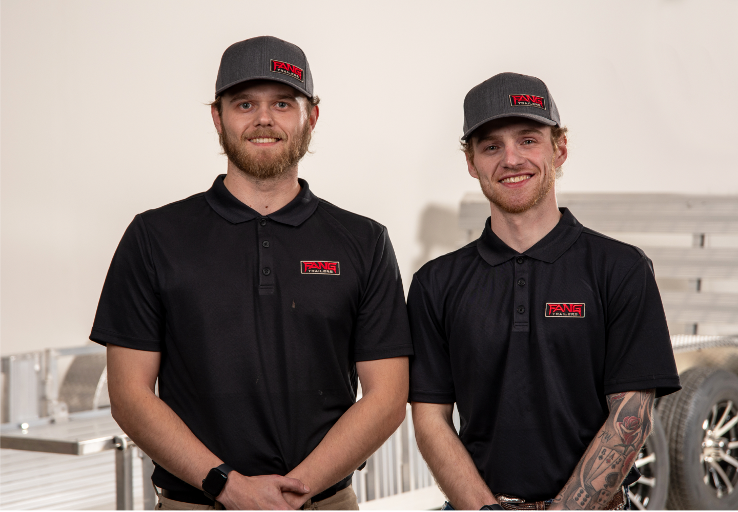 Brothers in black polo shirts with red fang logo wearing grey Fang logo hats with aluminum trailers behind them